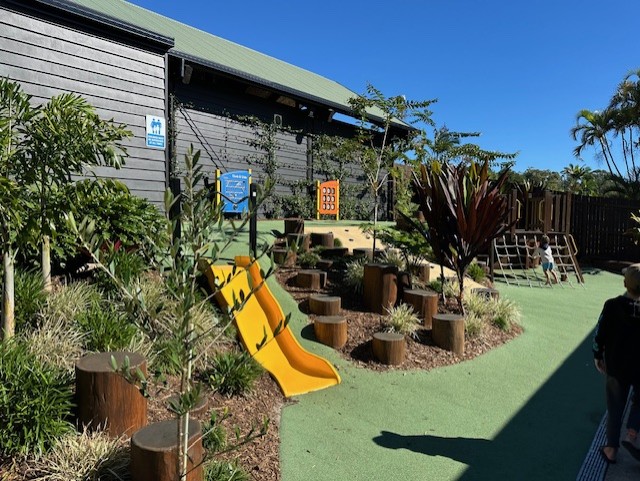 Nature play setting with yellow slide and timber play elements.